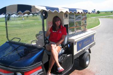 Smiling woman sitting in drivers seat of golf course drink cart.
